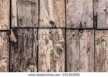 Very old, weathered, rotten floorboards, fixed and patched with planks of different origin, with uneven in-between gaps, large wood knots, and round head machine screws embedded - detail.