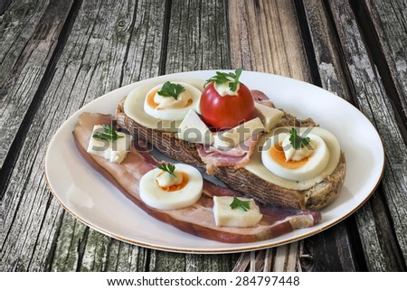 Toasted Integral Bread Sandwich, with Belly Bacon rasher, Ham, Egg slices, Cheese, Cherry Tomato and Mayonnaise, in White Porcelain Plate, on Old Cracked Wood Background.