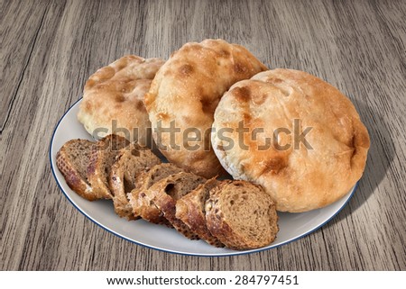 White porcelain plate with three Pita Bread loafs and Baguette Integral Brown Bread slices, on old, weathered, Wooden Table surface.