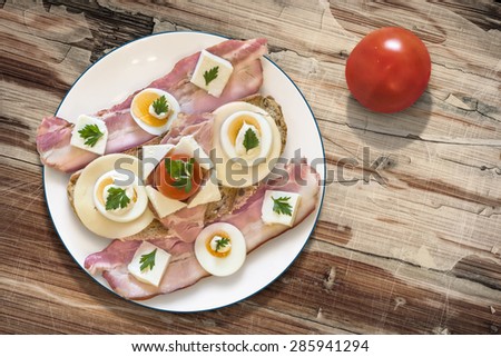 Toast Sandwich on porcelain plate, with  Ham, Cheese, hard boiled Egg slices, Cherry Tomato, Mayonnaise, Parsley leaves, and two extra Pork Bacon Rashers, on old, cracked, peeled Wood Background.