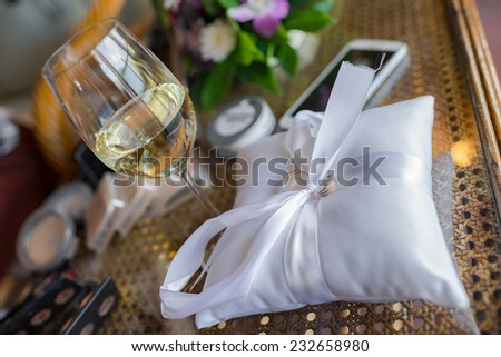 Wedding ring for bride and groom are bounded with a mini pillow and a glass of wine