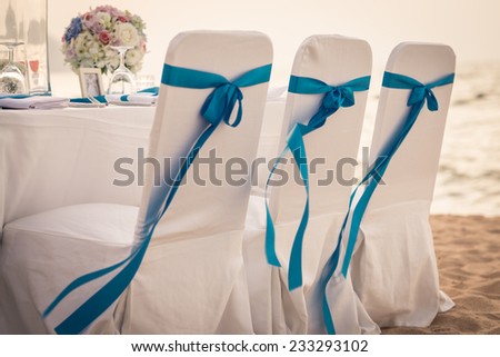 Decorated chairs at dining table on the beach for special guests at a wedding ceremony.