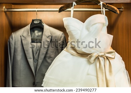 Bridegroom dress and bridal gown hanging in wardrobe