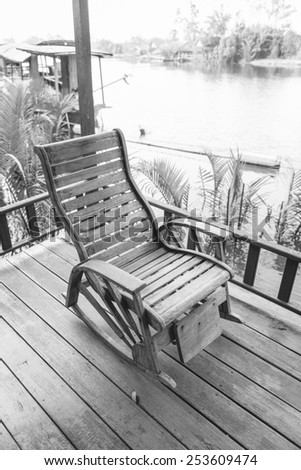 Old wooden rocking chair at balcony near the river in black and white photo