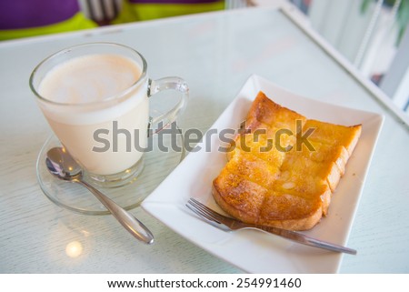 Bread toast with butter and condensed milk in white plate served with a cup of hot milk