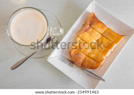 Bread toast with butter and condensed milk in white plate served with a cup of hot milk