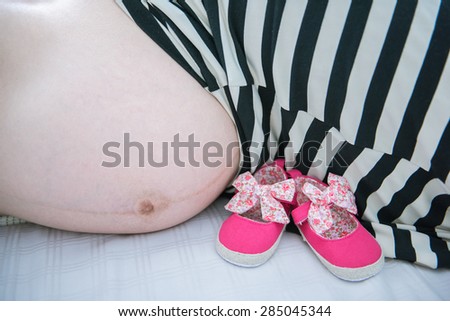 Pregnant woman and her pink baby shoe. Pregnant Woman Belly. Pregnancy