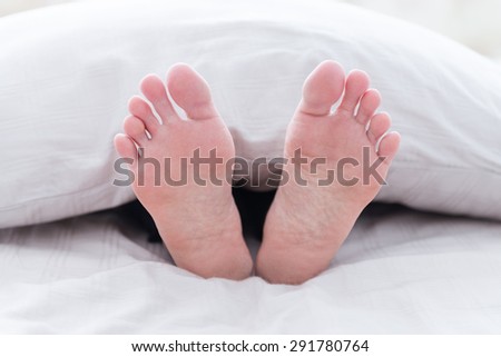 Human lie on bed with white sheets; focus on feet