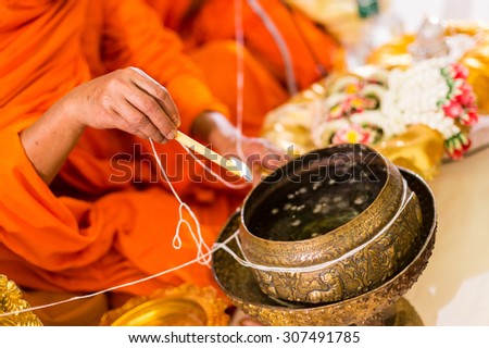 close up of buddhist monk\'s hand pouring melt candle tears to the water for making blessing water