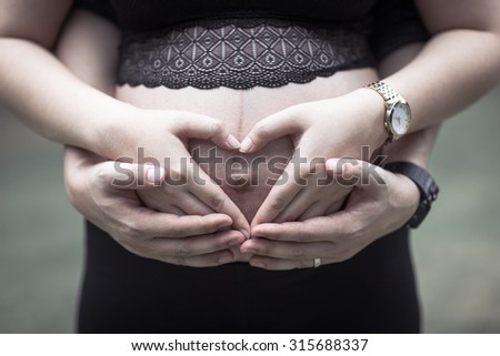 Happy pregnant couple hugging. Man and woman expecting for childbirth.Portrait of happy family. Making heart shape with hands on belly of pregnant woman. Male and female hands. Unrecognizable people