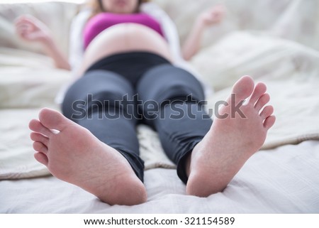 Closeup pregnant woman\'s feet on the bed, focus on her feet