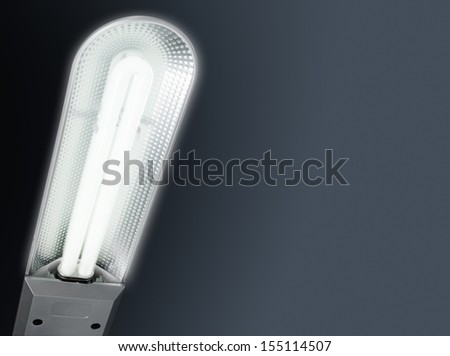 A PL-type energy saving lamp lighting in a table lamp on a cold gray gradient background.