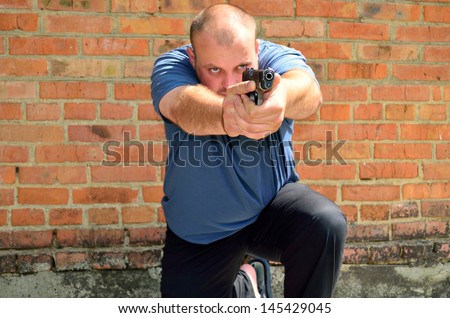 man on his knee with a pistol in his hand on a brick wall