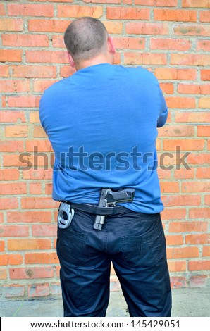 man standing back with a pistol and handcuffs in his belt on a brick wall