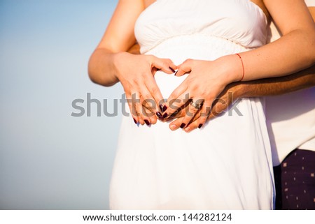 heart sign on pregnant tummy, hands of woman and man