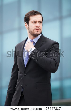 businessman fixing his tie looking serious in front of an office businessman