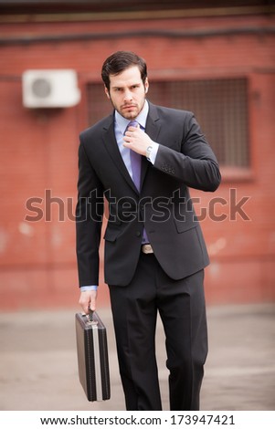 serious businessman walking on the street and fixing his tie