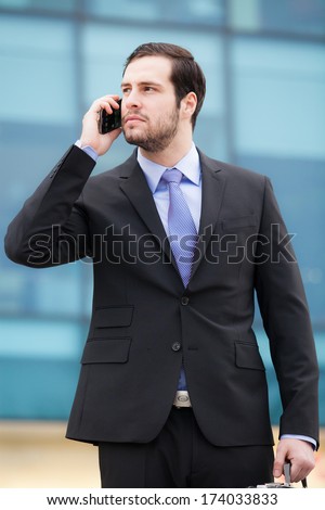 handsome businessman talking on the phone in front of an office building with a briefcase in hand