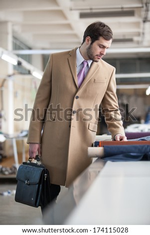 Business man wearing a business coat and briefcase in a textile factory chechink quality