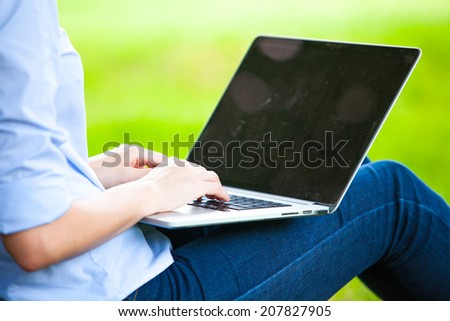 Young woman with laptop sitting on green grass in the park and relaxing