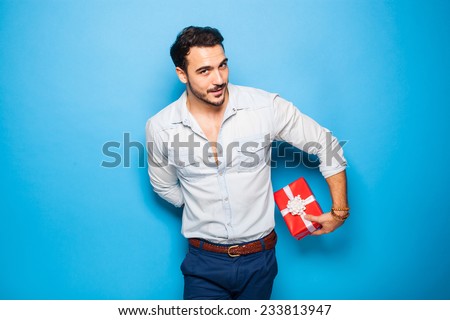 cute guy hiding a christmas gift behind him on blue background