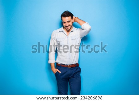 handsome man smiling with hand on head next to a blue wall
