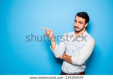 handsome man with beard pointing in one direction on a blue background