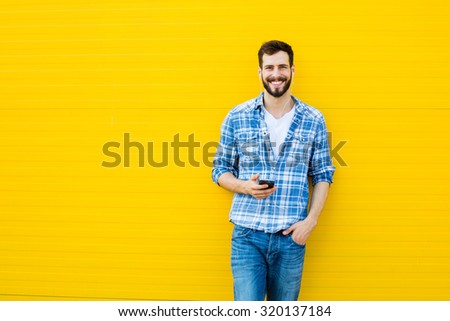 young happy man casual dressed with headphones and smart phone on yellow background