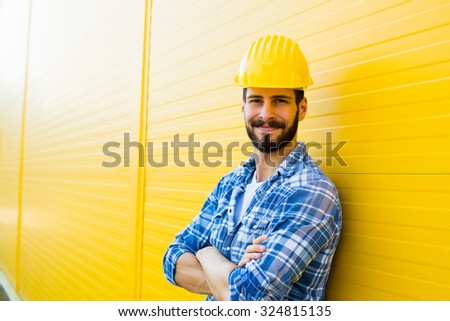 worker with helmet and yellow plaid shirt near a wall
