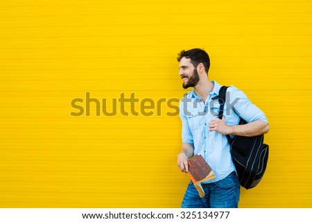handsome student with backpack standing outside on yellow background