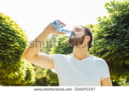 close up of a man drinking water from a bottle outside