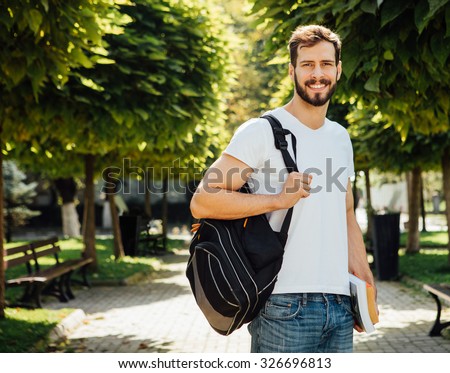 handsome student having books in hands and backpack standing outside