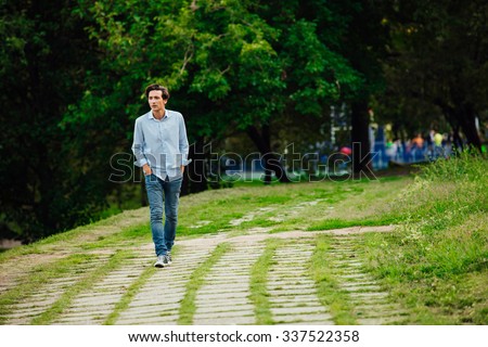 young adult in blue shirt and jeans walking alone in park
