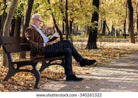old elegant man with gray hair reading a book outside in park