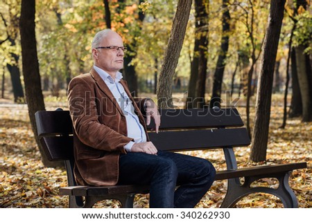 elegant old man with white hair sitting and thinking on a bench outside