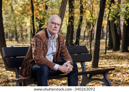 elegant old man with white hair sitting and thinking on a bench outside