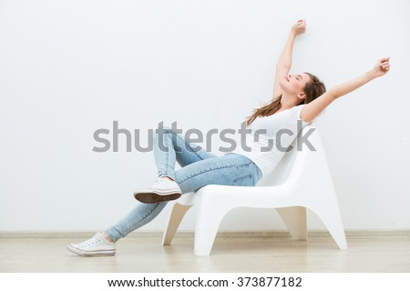 single happy young woman sitting on a white chair in an empty room, thinking on something