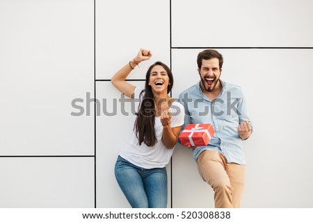 young happy couple standing outside, man offering a gift to his girlfriend and making her very happy