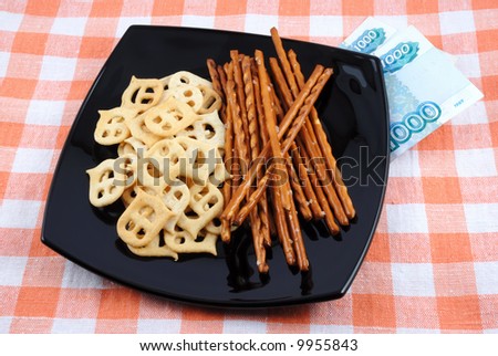 Mini crackers and salty grain sticks to beer on a black plate and money