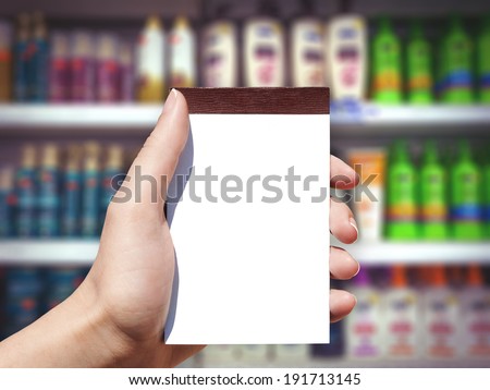 white blank vertical notebook in woman hand and shampoo background