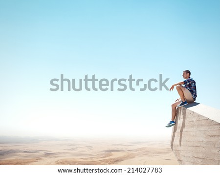Young man sitting on a cliff and looking at the desert
