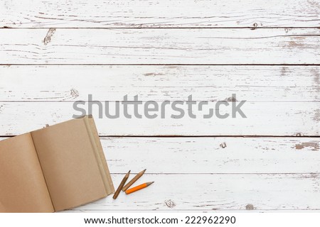 white wooden table with craft grunge notebook and a pencil in a corner, top view