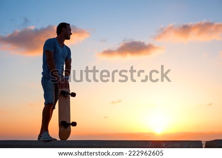 man silhouette with skateboard near the ocean in sunset