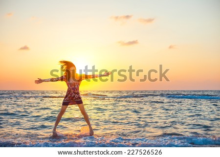 young and beautiful girl in colorful dress jumping like a star in ocean water in sunset