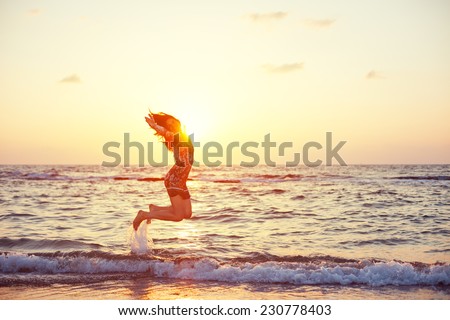 young and beautiful girl in colorful dress jumping in ocean water in sunset