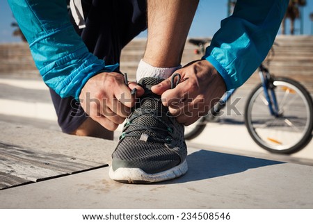 preparation of sportsman tie shoelaces on his running shoe and mountain bicycle at background
