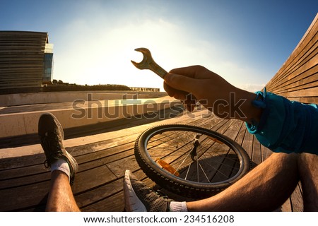 cyclist sitting and resting with the wrench in his hand and the mountain bike wheel at the sunset, POV view