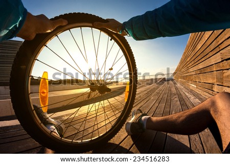 cyclist sitting and resting with the wheel of mountain bike in his hand at the sunset, POV view