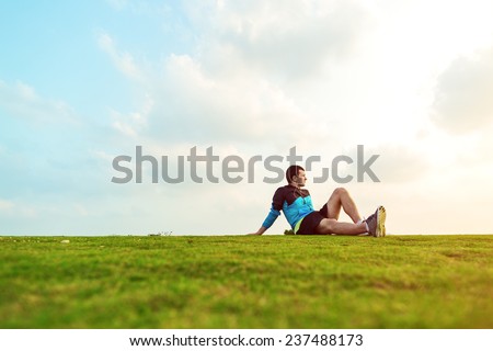 athletic sportsman resting after sport in the park and looking far away at the sunset