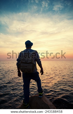 traveler with backpack near sea looking far away at horizon at sunset